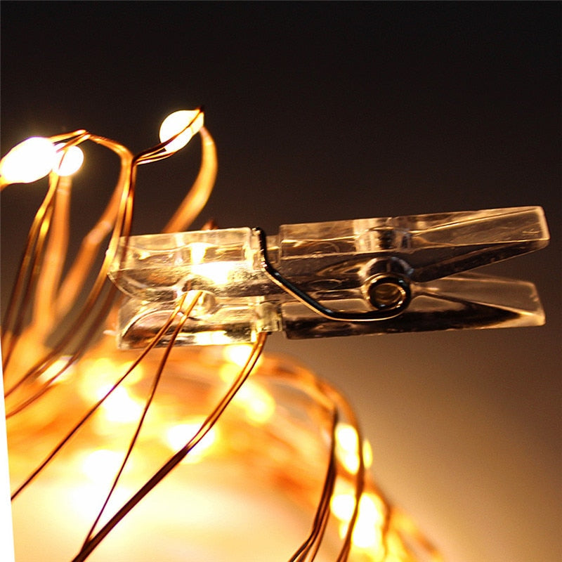 A close-up of a clear plastic clip from a string of clip lights, illuminated with a warm glow, highlighting the details and transparency of the clip against a dark background.