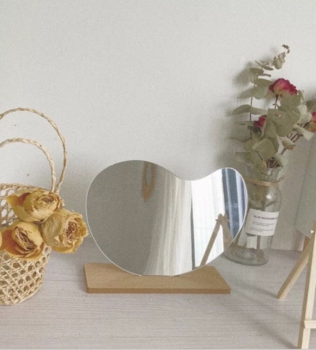 An aesthetically pleasing scene with the cloud-shaped mirror standing on a wooden block, accompanied by a dried flower bouquet in a net bag and a glass vase, suggesting a nature-inspired room decor.