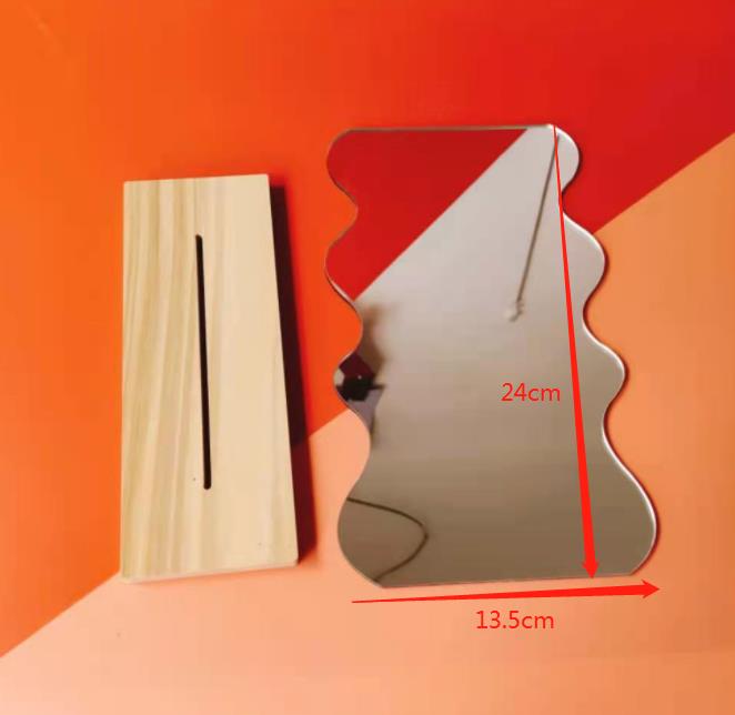 A wavy-edge mirror standing in a wooden base, measured at 24cm by 13.5cm, casting a reflection against an orange backdrop, showcasing a playful and creative design.