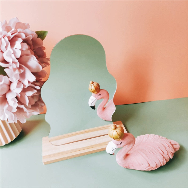 A silhouette-style mirror on a wooden base featuring a feminine room decor with soft pink flamingos and golden ornaments, complementing a pastel-colored room.