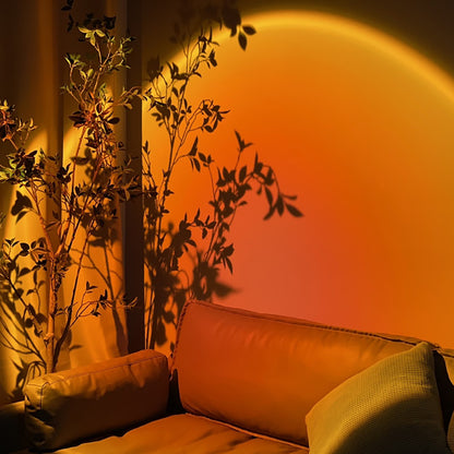 A vibrant orange hue cast by a sunset projector on a wall with a leather sofa, creating a relaxing room decor with silhouetted plant shadows adding a nature-inspired touch.
