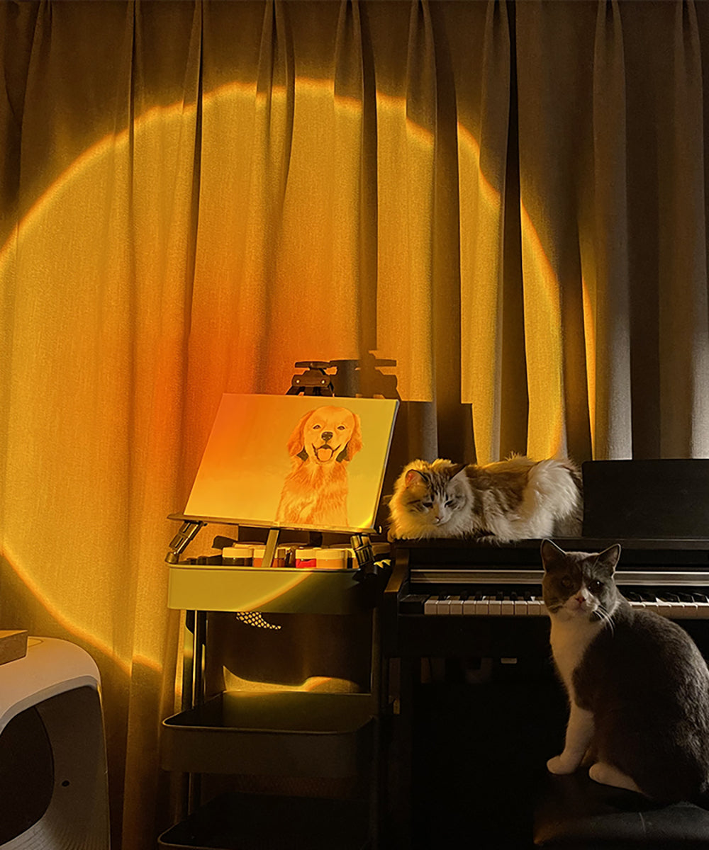 A cozy room illuminated by a warm sunset glow from a projector, highlighting a painting of a golden retriever on an easel, with a fluffy cat perched on a digital piano, and another cat sitting in front.