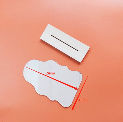 A wavy-shaped mirror with dimensions of 24cm by 15cm laid flat next to a wooden block with a slit, on an orange background, embodying a minimalistic and functional design.