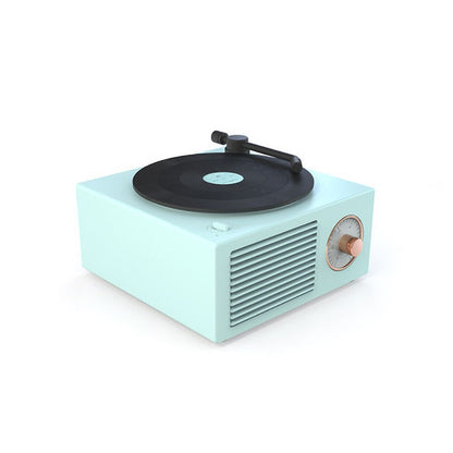 A compact and minimalist white retro-style Bluetooth speaker with a vinyl record design on top. The speaker has a simple black tonearm and a single copper-colored control knob on the front.
