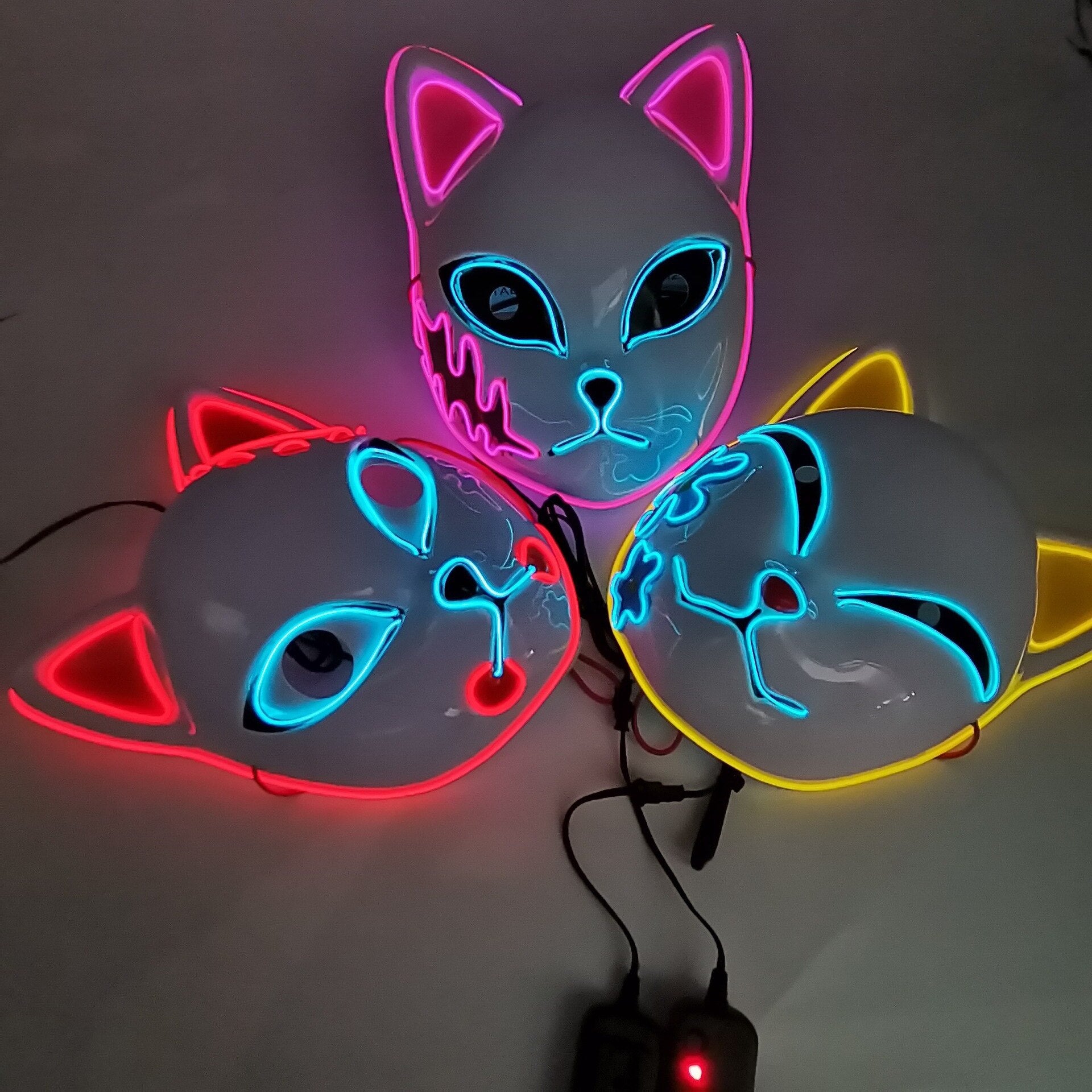 A dark setting showcasing three Anime Style Cat Masks illuminated with different neon LED colors, highlighting the masks' vibrant glow-in-the-dark feature.