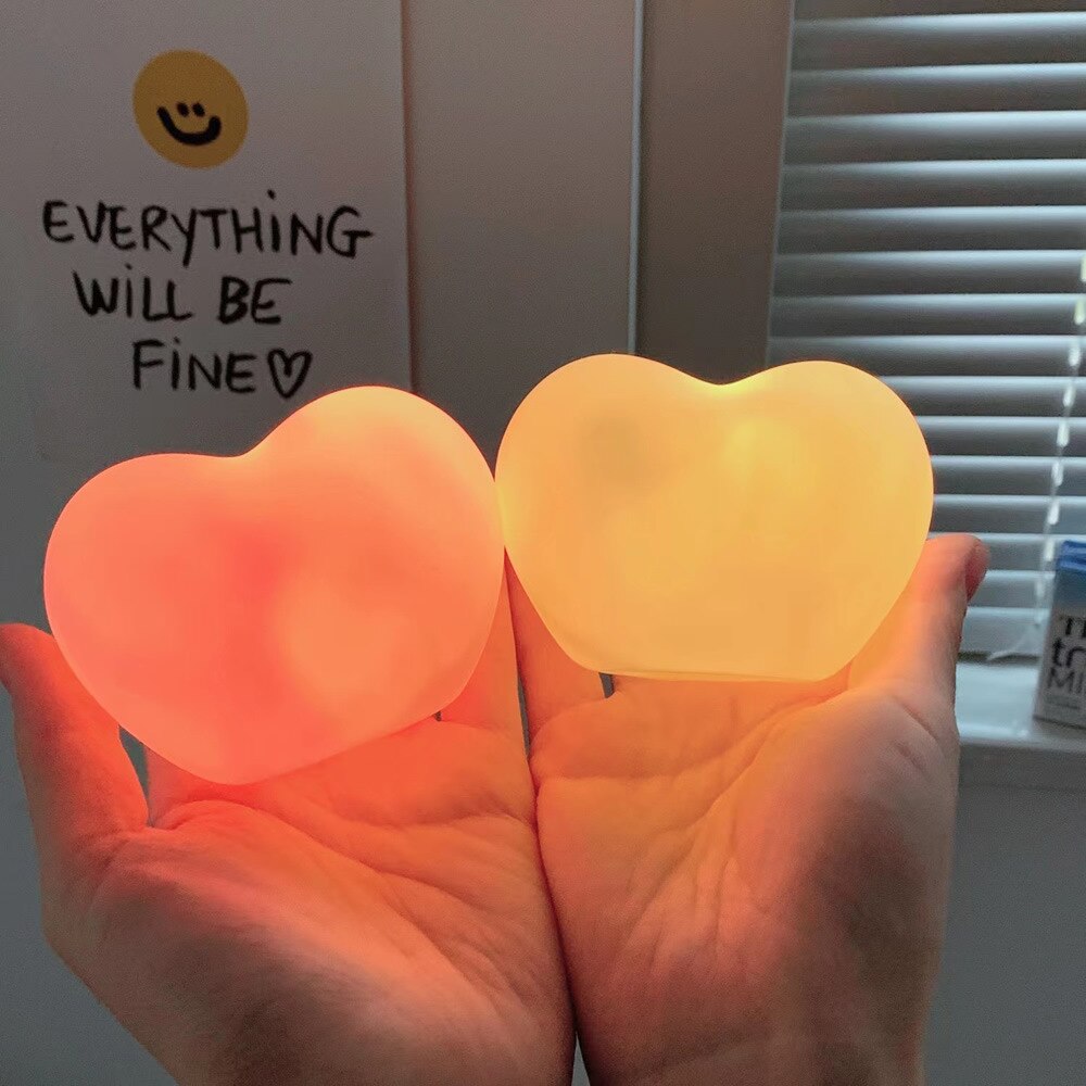Hands gently cradling two heart-shaped lamps, one glowing with a soft red and the other with a yellow light, conveying a message of hope and comfort as part of the 'relaxing-room-decor' and 'gift-ideas' collections.