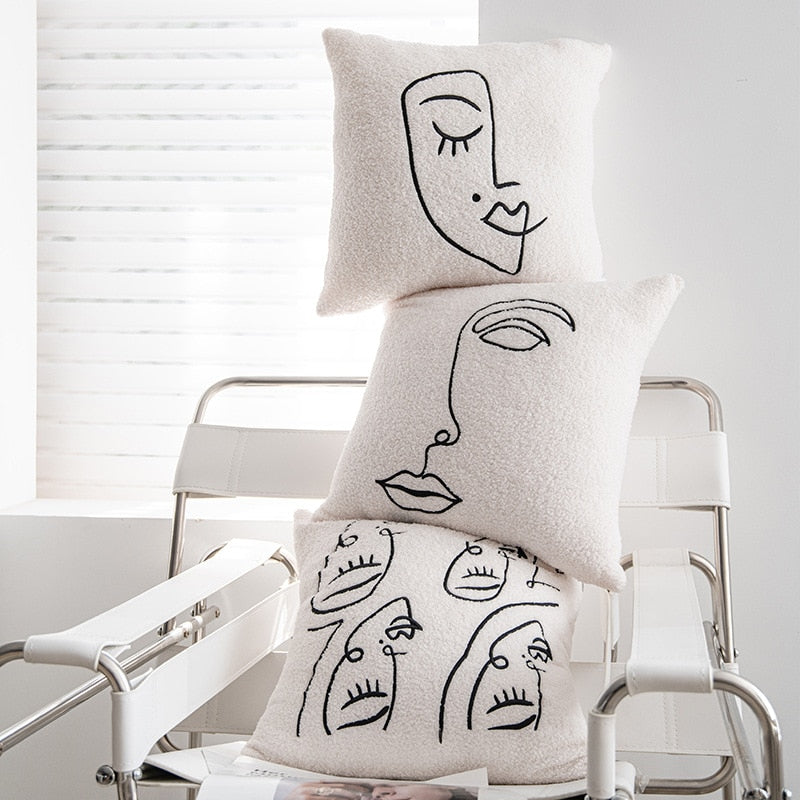 Three plush pillowcases stacked on a modern metal chair in a bright room with white blinds. Each pillowcase features a unique, abstract black line drawing of a face, showcasing different expressions, reflecting the 'Art Hoe' aesthetic. These pillowcases are well-suited for a variety of decor themes such as 'Boho', 'Coquette', 'Cottagecore', 'Danish Pastel', and would add an artistic touch to any 'Dorm Room', 'Dreamy', 'Feminine', or 'Relaxing Room' decor.