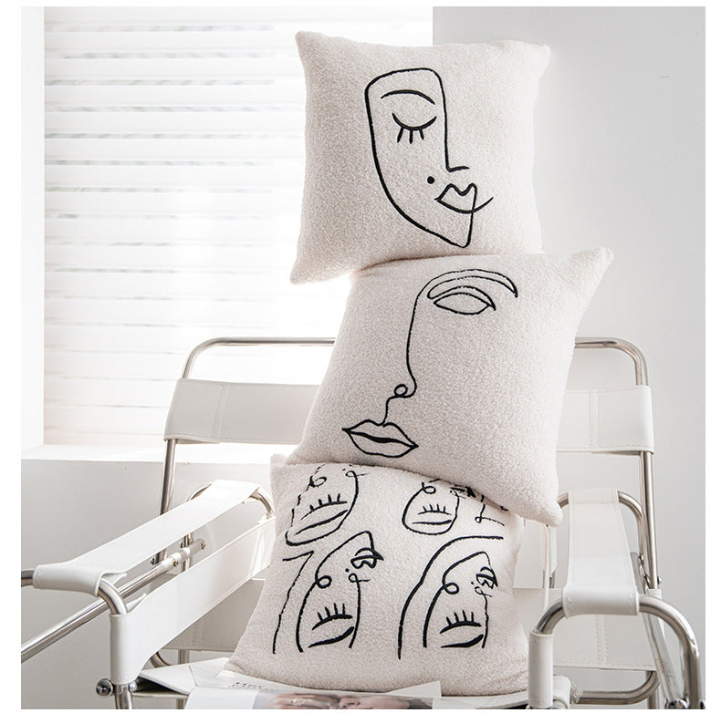 An image of a modern, airy room with a stack of three artfully designed pillowcases placed on a sleek metal chair. Each pillowcase has a unique, abstract line drawing of a face, rendered in black on a cream-colored background, embodying the 'Art Hoe' design aesthetic. This scene is complemented by the soft natural light filtering through white blinds
