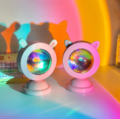 Two Sunset Light Projectors with cat ears displayed against a rainbow-colored wall from the kawaii room and cottagecore room decor collection. The projectors cast vibrant, colorful shadows, perfect for an art hoe room decor setting.