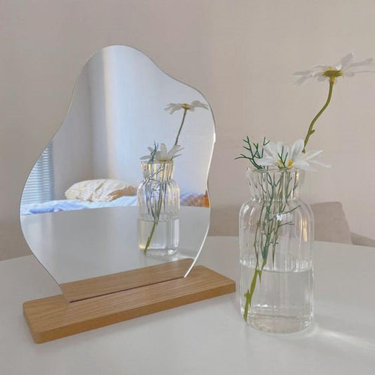 A gently curved mirror on a wooden stand reflecting a serene and relaxing room decor with white daisies in a clear vase, suitable for a minimalistic or Danish pastel decor.
