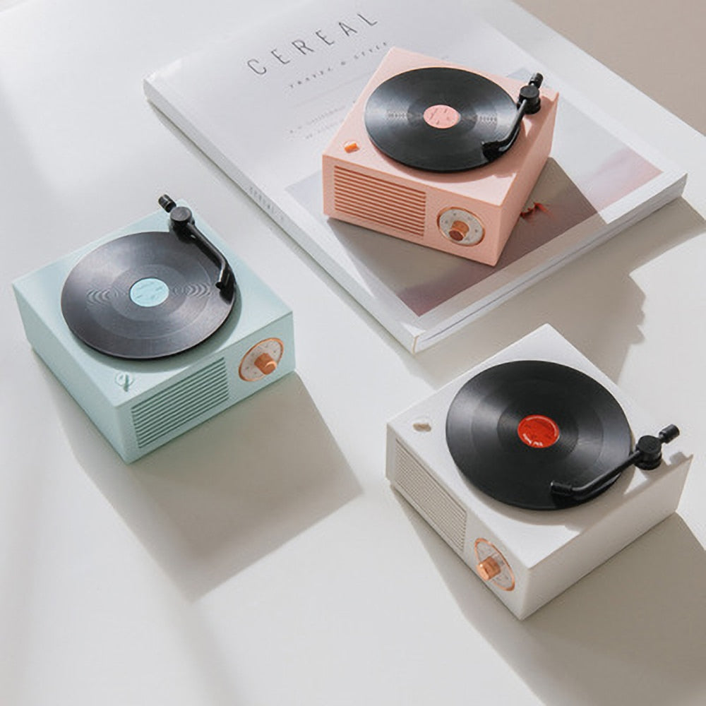 An array of retro Bluetooth speakers in white, mint green, and pastel pink, each with a vinyl record design on top. They are placed on top of a book, with a simple tonearm and front-facing speaker grille, showcasing their variety in a clean and modern setting.